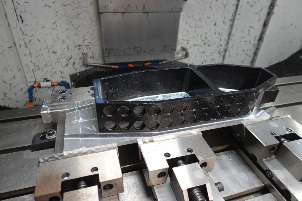Châssis en aluminium usiné sur une machine CNC, maintenu par des étaux industriels pendant une opération de fraisage de haute précision, avec un motif hexagonal visible sur la pièce mécanique.