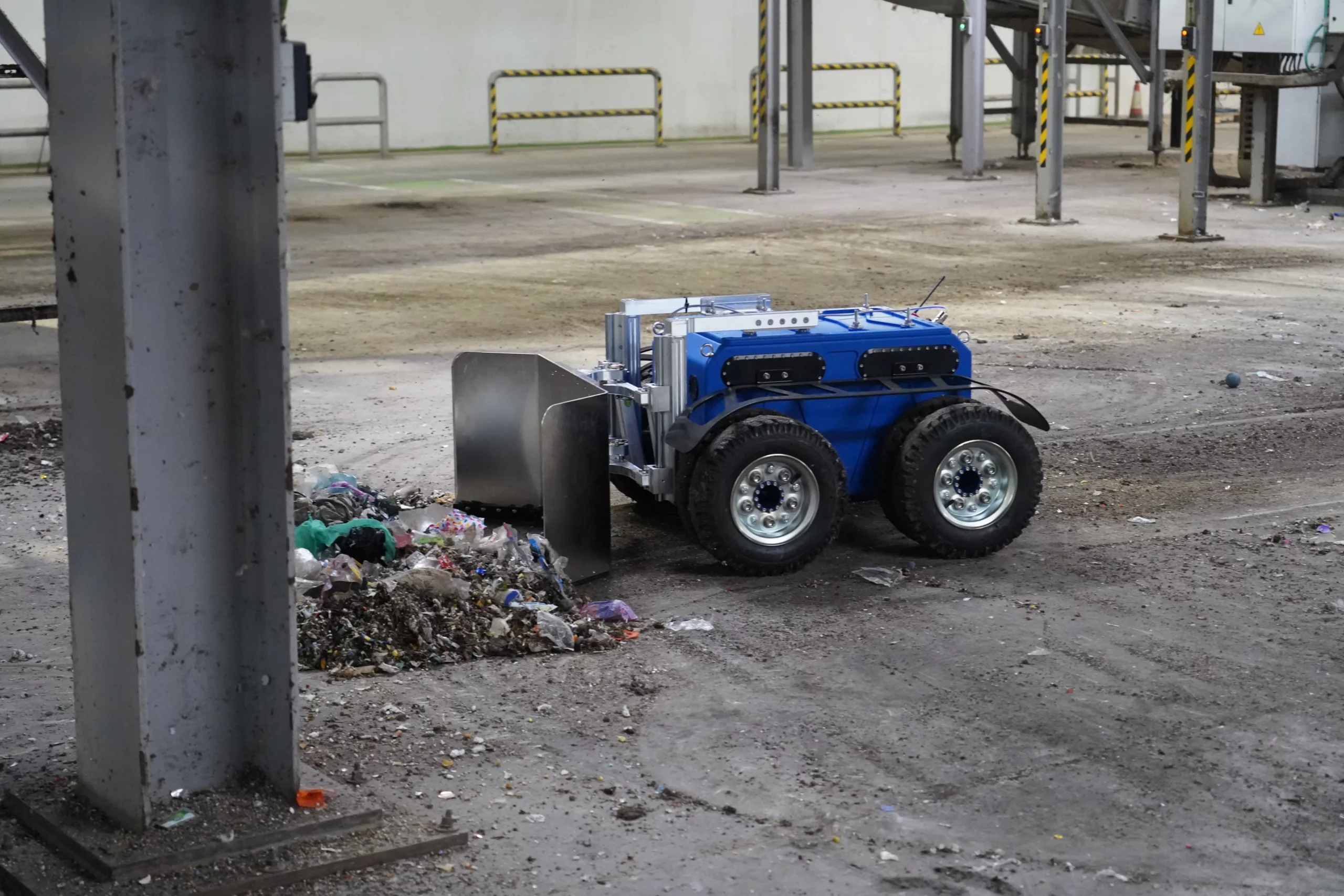 Robot Quator de Sfynx Industry en démonstration dans une déchetterie, utilisant sa lame frontale pour pousser et regrouper des déchets au sol. Le robot tout-terrain à quatre roues illustre l’automatisation des opérations de nettoyage et de manutention dans les centres de tri et environnements industriels.