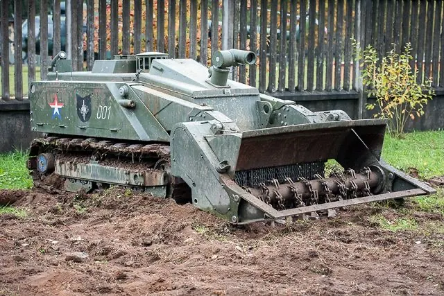 Robot terrestre blindé équipé d’un système de déminage à l’avant, en train de labourer le sol dans une zone extérieure, illustrant un véhicule militaire téléopéré conçu pour le génie, le déminage et les opérations de terrain à haut risque.
